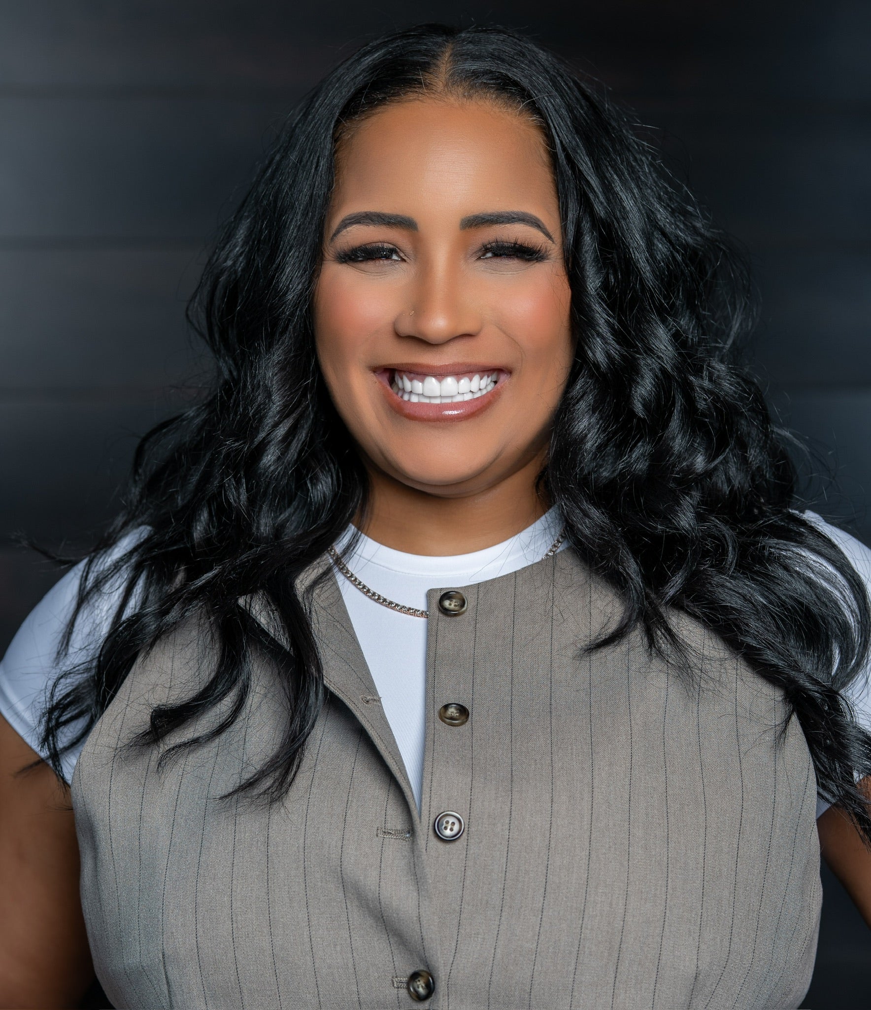 Woman wearing a beige vest over a white shirt against a dark background