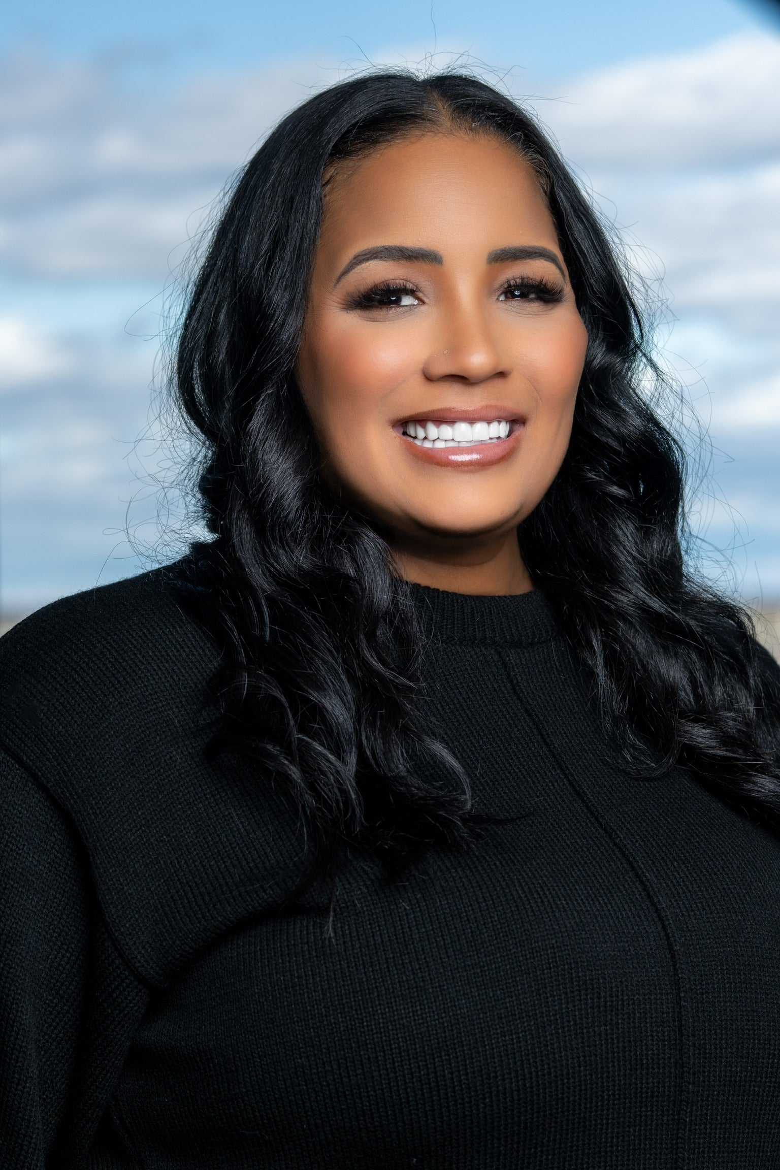 Woman with long black hair wearing a black sweater against a blue sky background