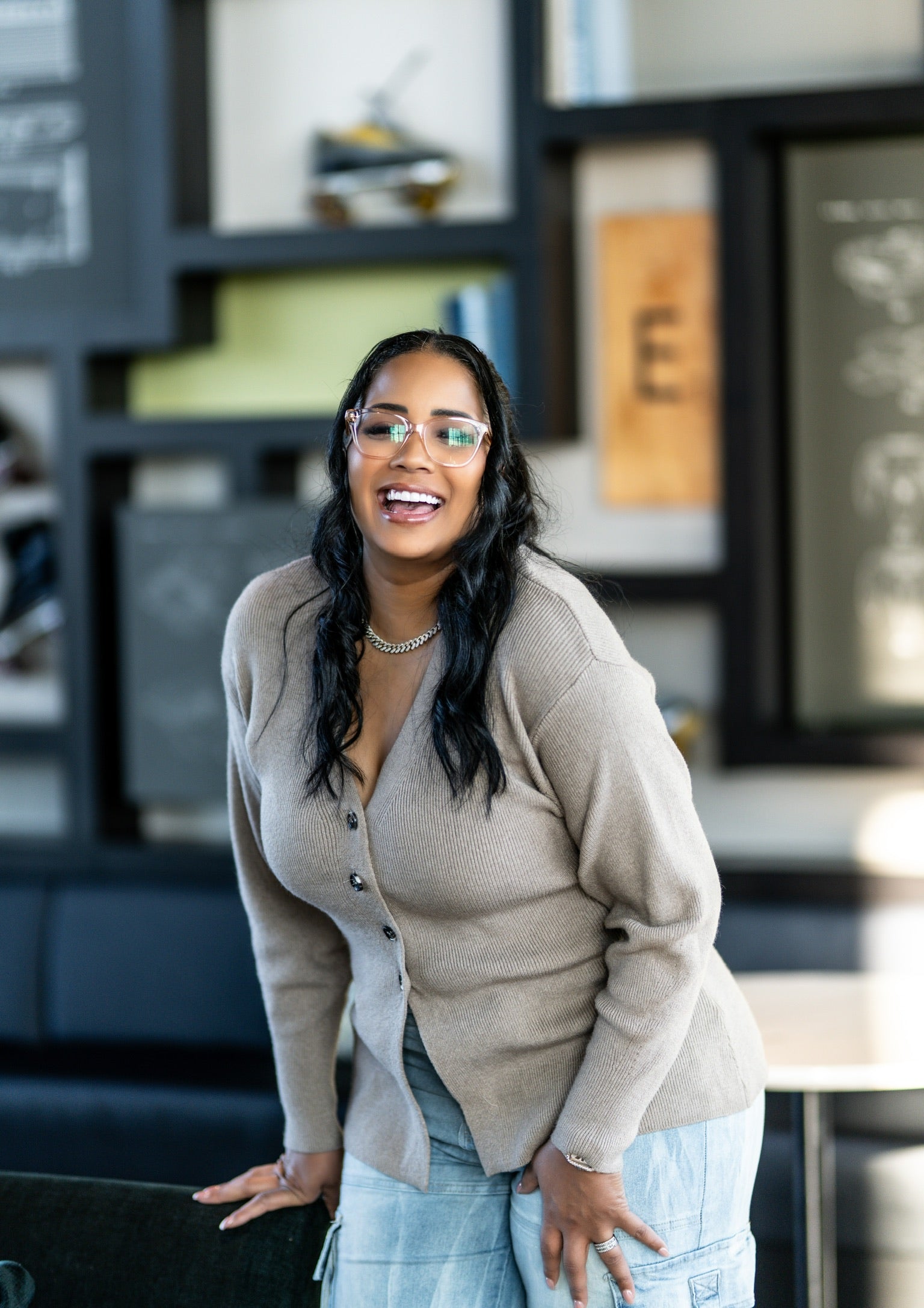 Woman in a beige cardigan and blue jeans standing in an office setting